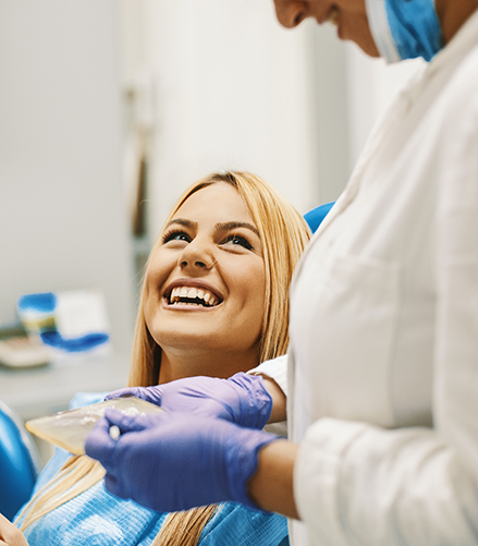 Woman in dental chair grinning up at her dentist