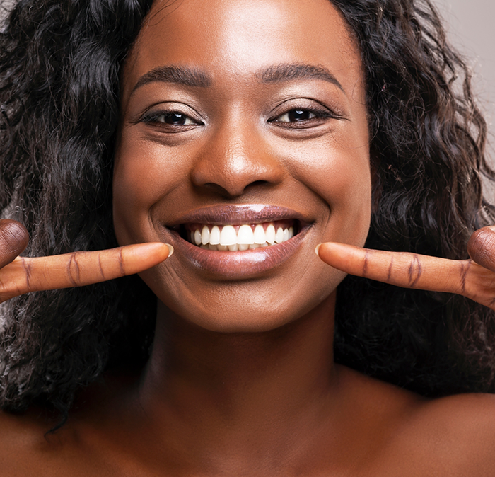 Woman pointing to her smile after cosmetic dentistry in Independence