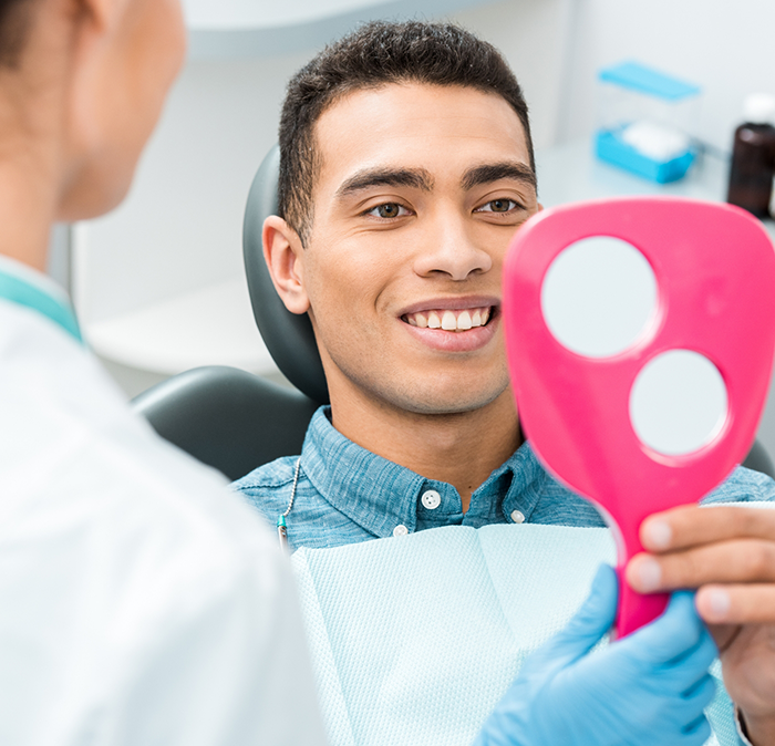 Man looking at his smile in a mirror after replacing missing teeth in Independence