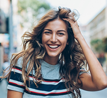 Woman on city sidewalk touching her hair