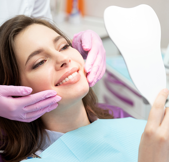 Young woman admiring her smile in a mirror after restorative dentistry in Independence