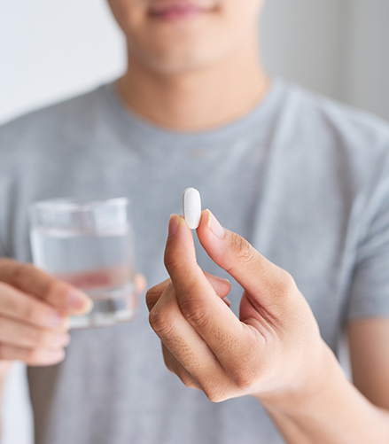 Person holding a glass of water and a white pill